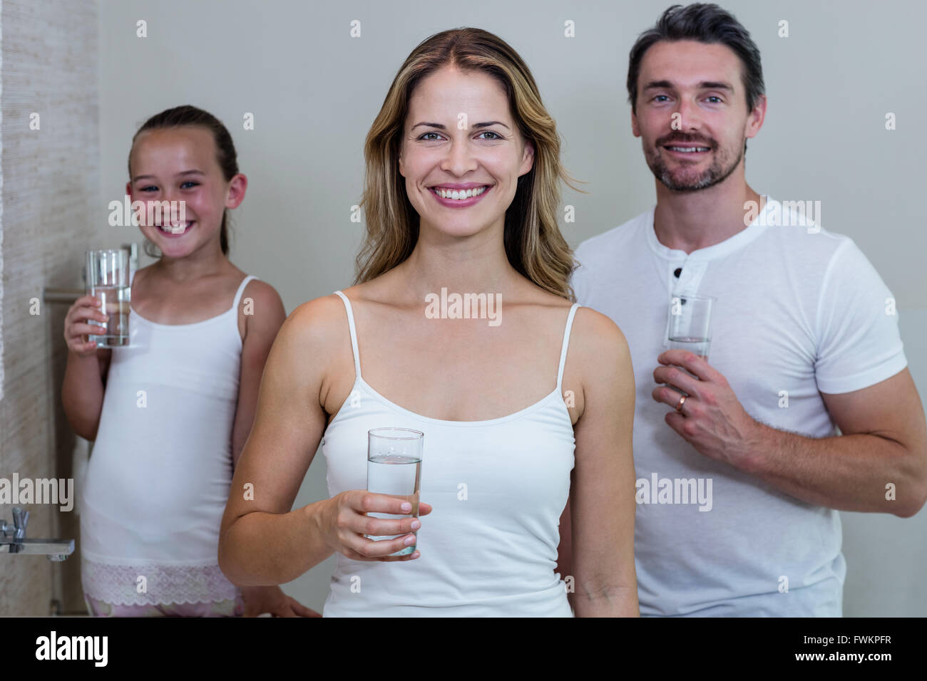 Les parents et la fille tenant un verre d'eau dans la salle de bains Banque D'Images