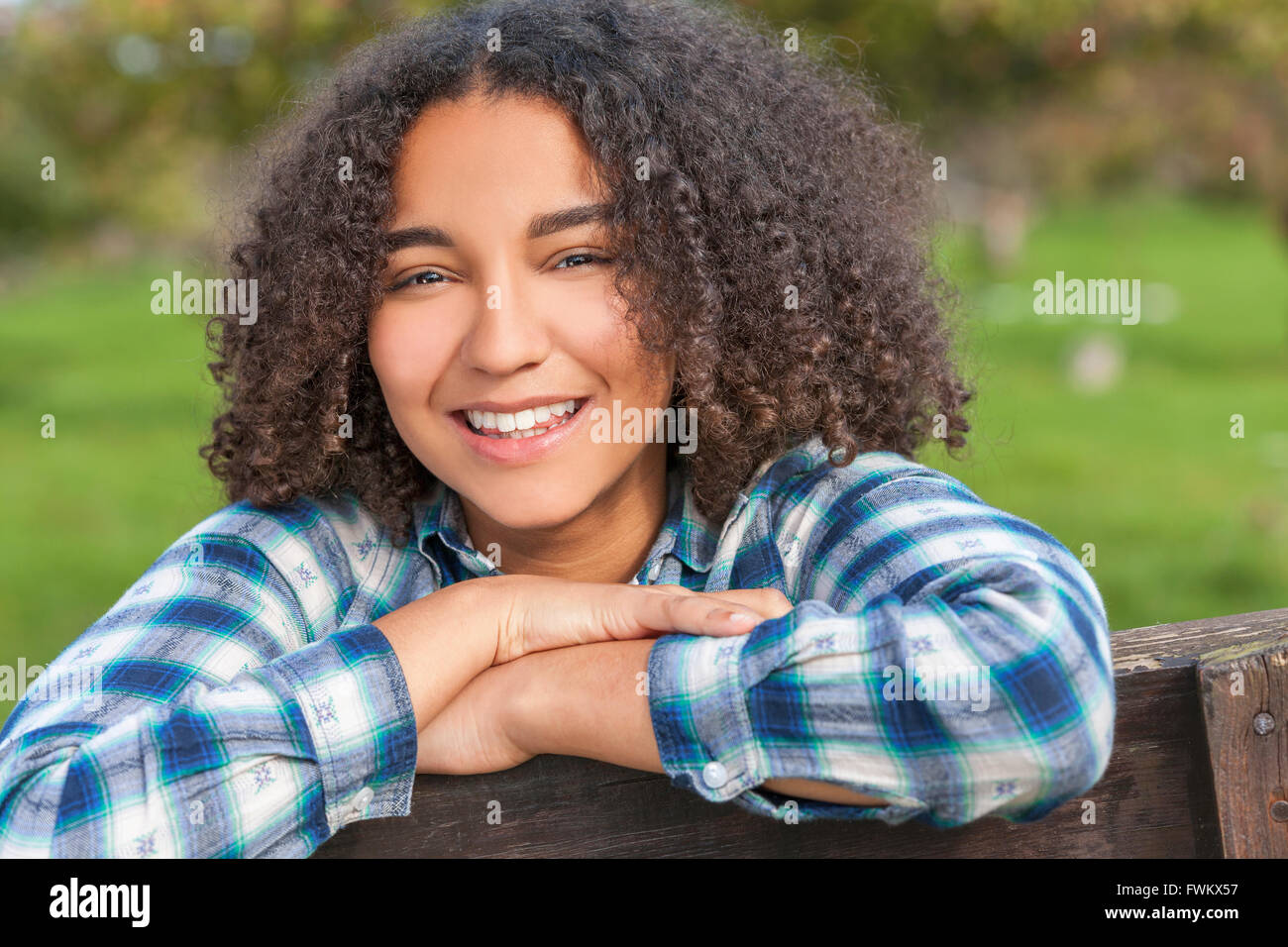 Portrait plein air de belle happy mixed race African American girl adolescent enfant féminin reposant sur une clôture campagne smiling Banque D'Images