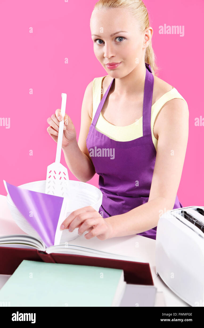 Jeune femme au foyer attrayant, cuit les aliments dans une cuisine rose Banque D'Images