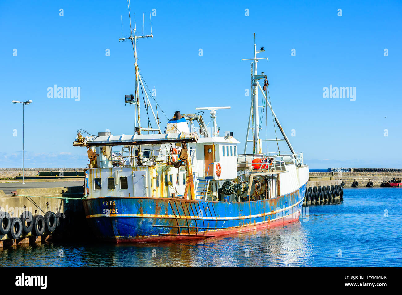 Simrishamn, Suède - 1 Avril 2016 : un bateau de pêche bleu et blanc amarré dans le port. Les pneus de voiture accrocher à l'embarcadère que bump Banque D'Images