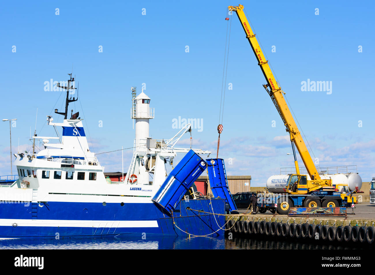 Simrishamn, Suède - 1 Avril 2016 : Grue mobile Liebherr jaune du levage d'une aile chalutier bleu du sol au niveau de l'orifice. Travail Normal Banque D'Images