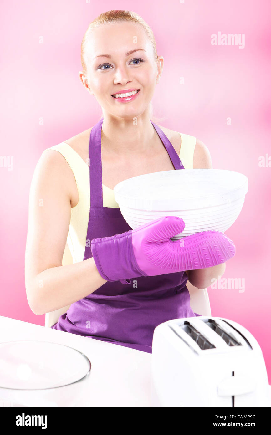 Jeune femme au foyer attrayant, cuit les aliments dans une cuisine rose Banque D'Images