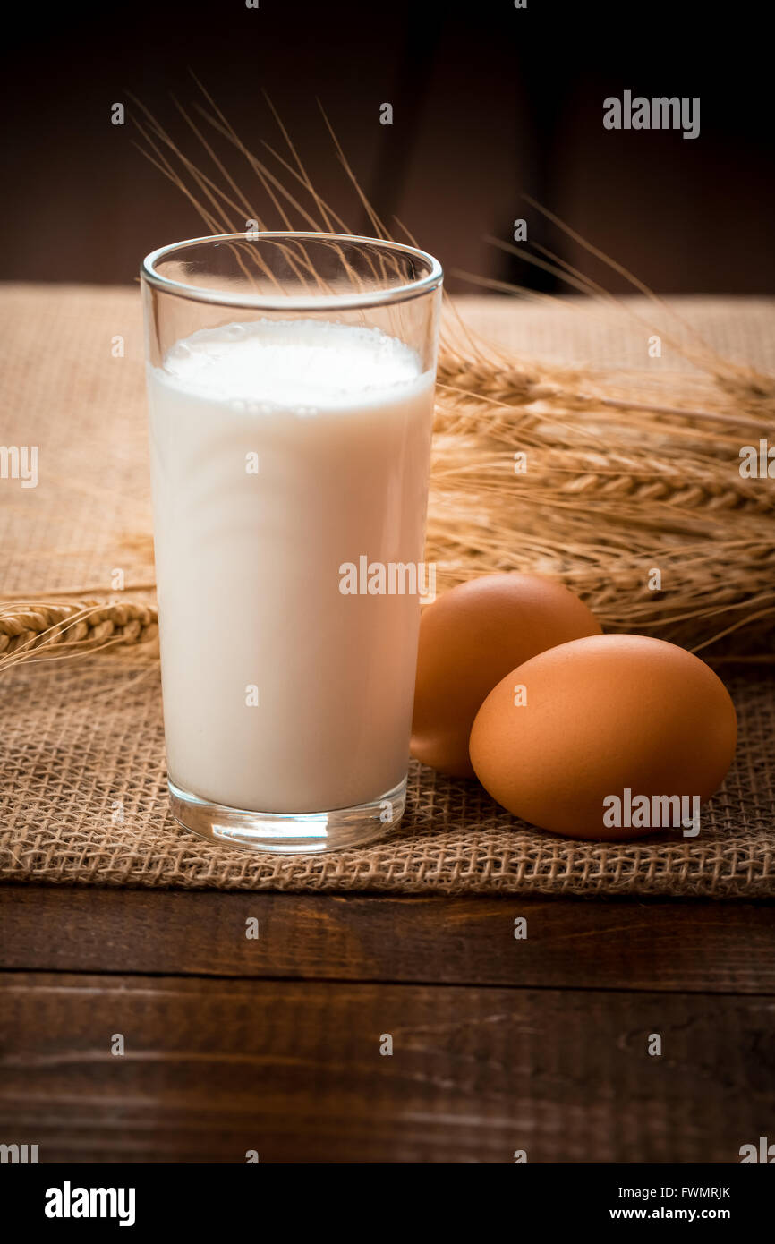 Verre de lait, deux œufs et les épis de blé s'allonger sur la serviette d'une toile sur la vieille table en bois Banque D'Images