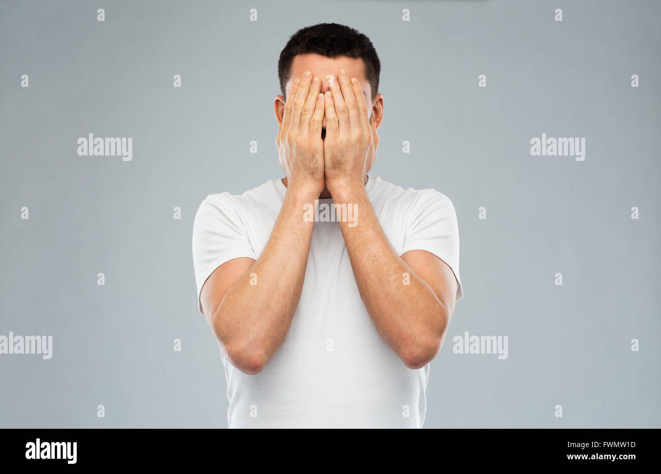 Homme en blanc T-shirt couvrant son visage avec les mains Banque D'Images