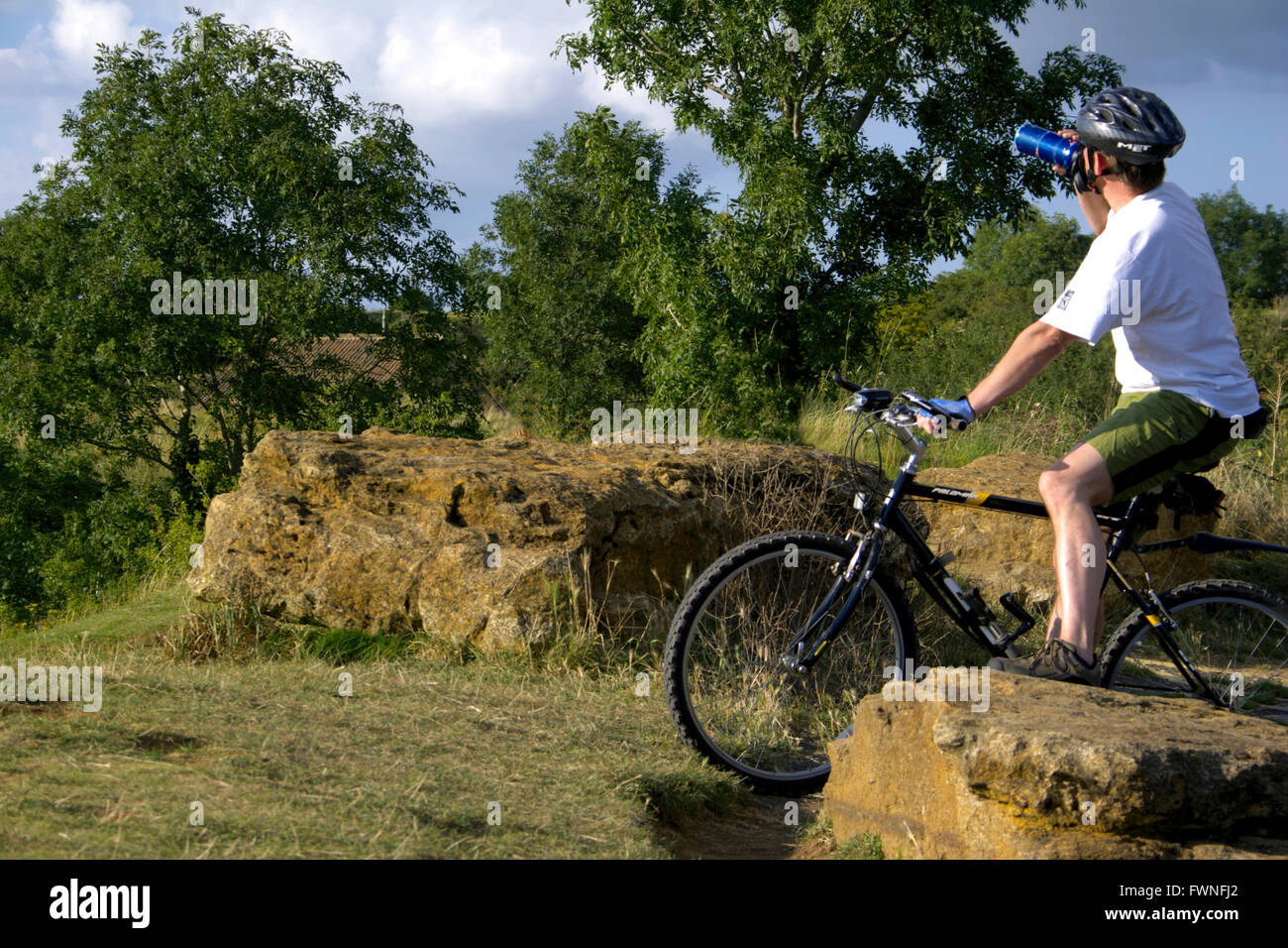 Cycliste sur Ham Hill, Somerset, Angleterre, les gens jeune homme reposant repose sur l'eau de boisson potable rock bouteille vélo assis Banque D'Images