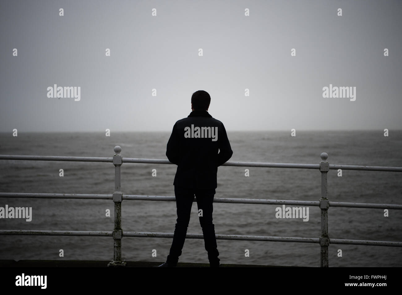 Une vue arrière d'un seul jeune solo homme debout face à la mer par une froide journée misérable couvert gris, UK Banque D'Images