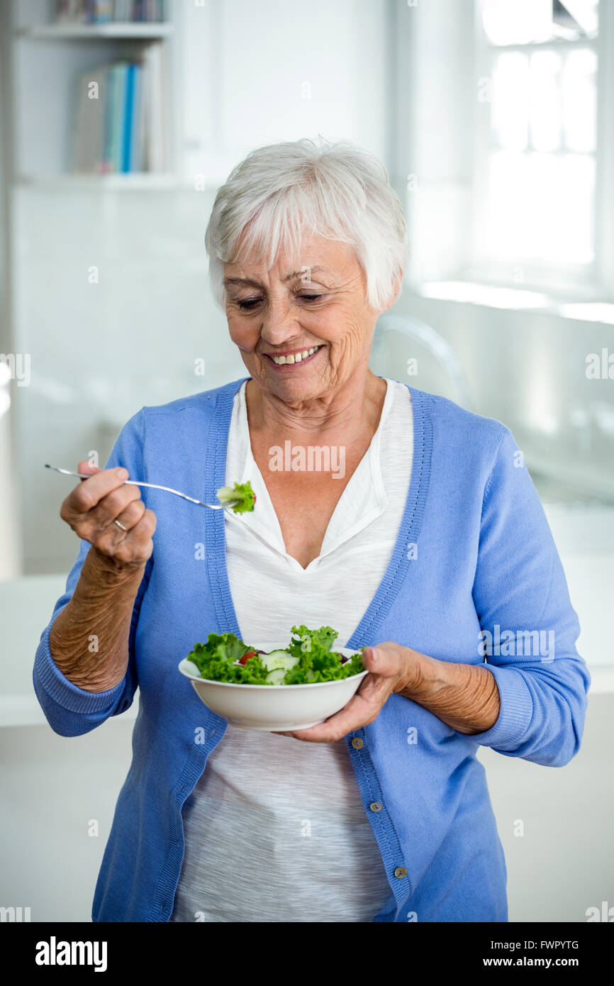 Senior woman eating salad en étant debout dans la cuisine Banque D'Images