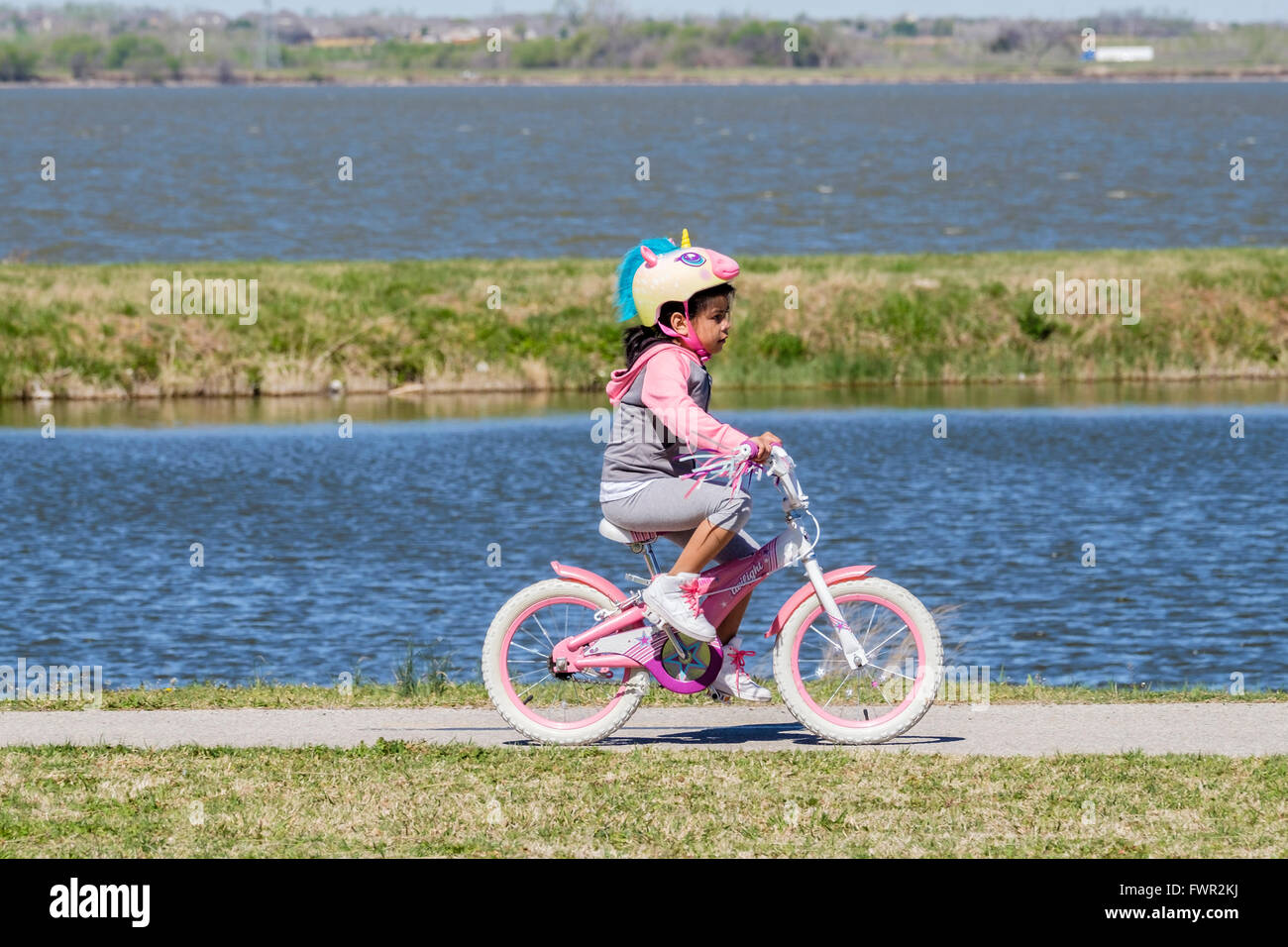 Une jeune fille hispanique avec une licorne helmit rides son vélo sur les sentiers du lac Overholser, Oklahoma City, Oklahoma, USA. Banque D'Images