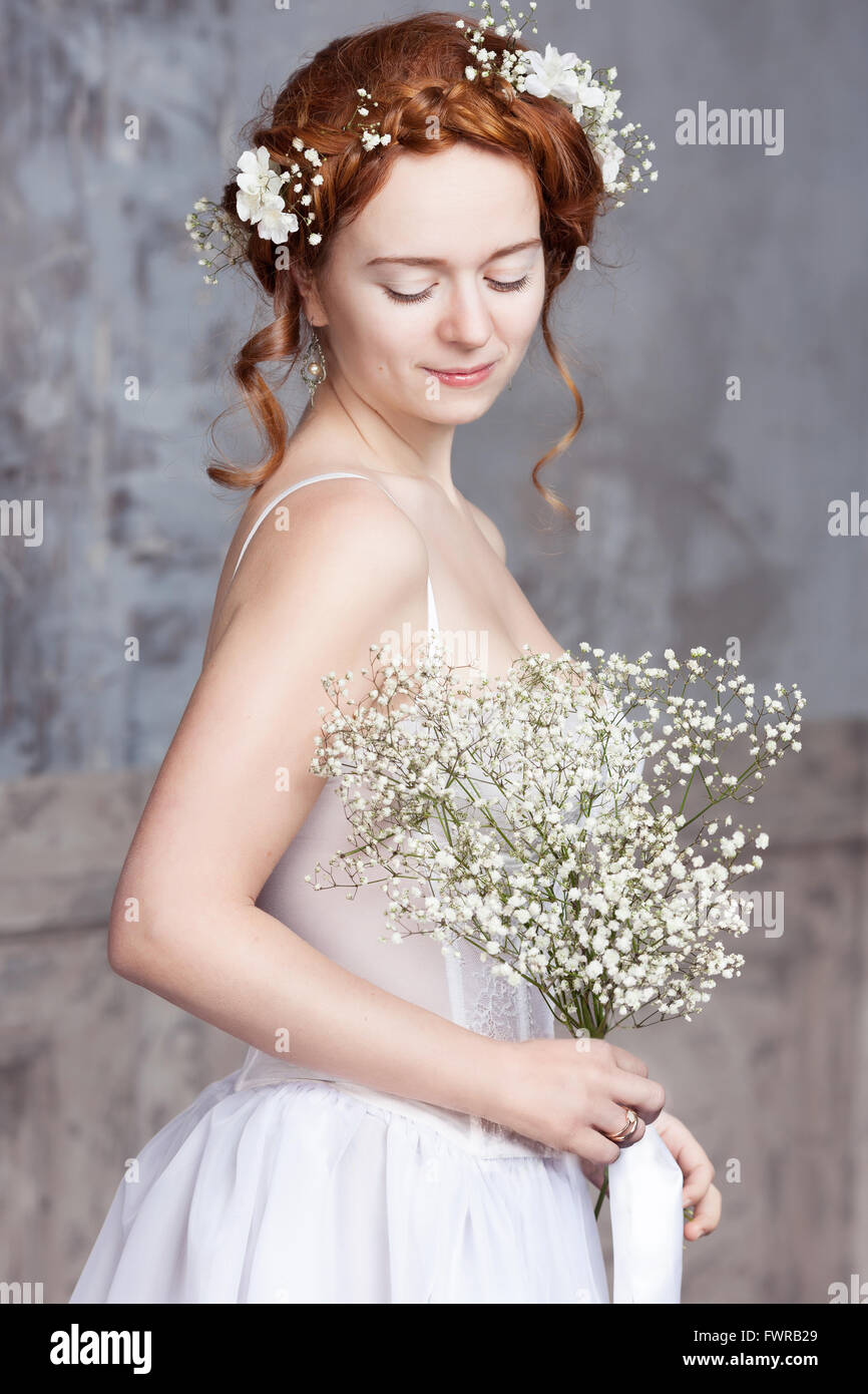 Les jeunes aux cheveux rouges en blanc mariée robe de mariage. Elle se lève, ses yeux sont fermés, elle rêve tient un bouquet de blanc Banque D'Images