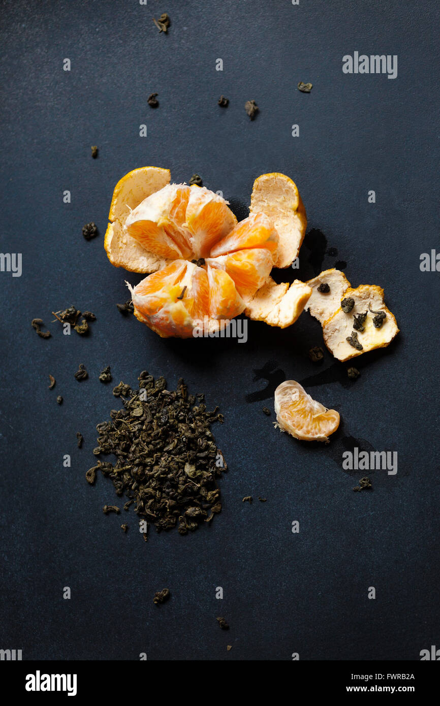 Peeled tangerine se trouve sur la carte. Il y a des gouttes de jus de mandarine, Peel et un éparpillement de thé vert autour. Le fruit est Banque D'Images