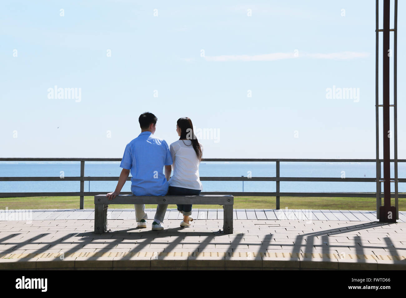 Jeune couple japonais assis sur un banc au bord de la mer Banque D'Images