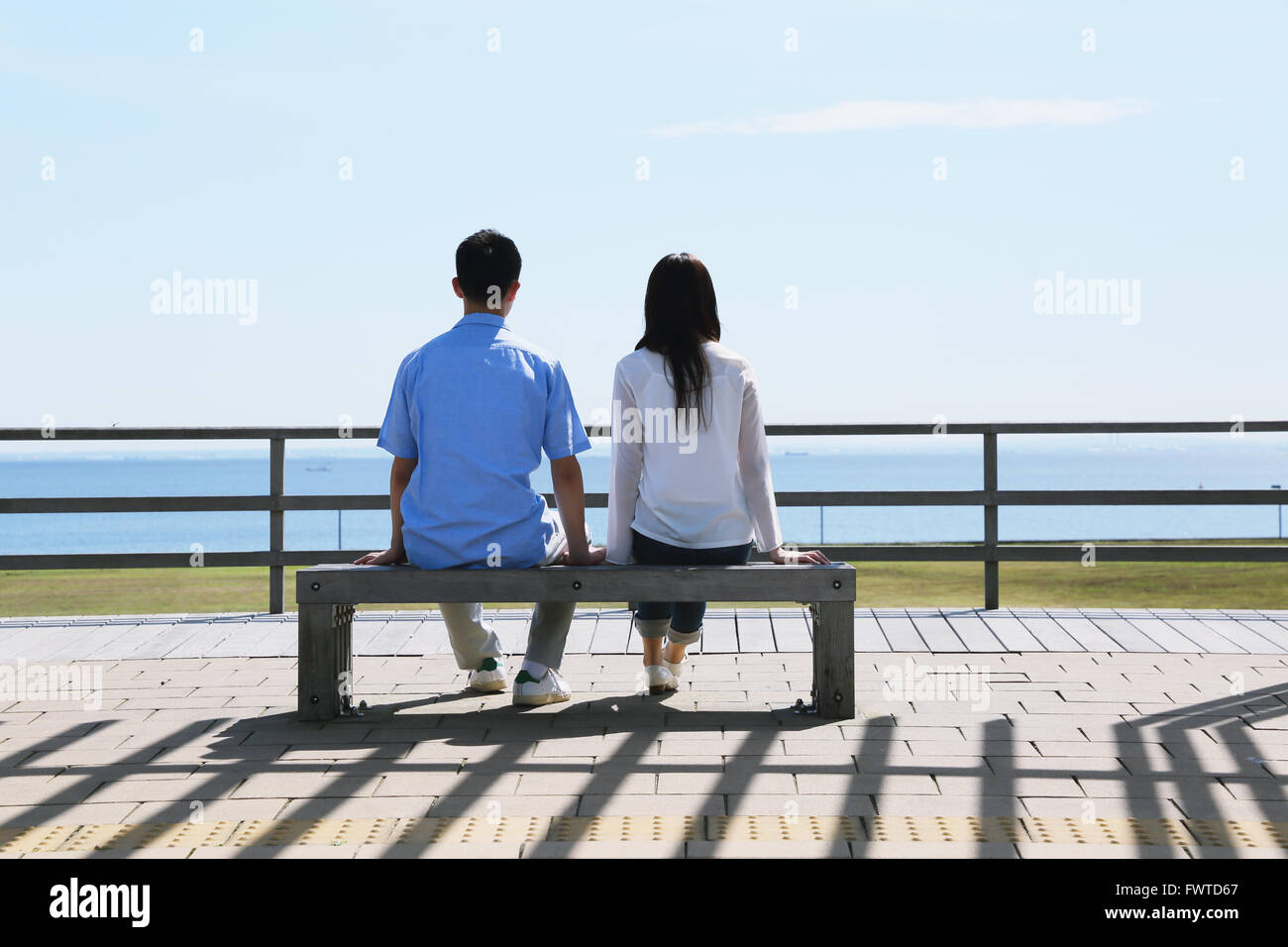 Jeune couple japonais assis sur un banc au bord de la mer Banque D'Images