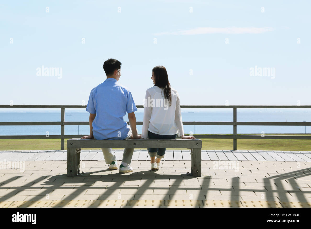 Jeune couple japonais assis sur un banc au bord de la mer Banque D'Images