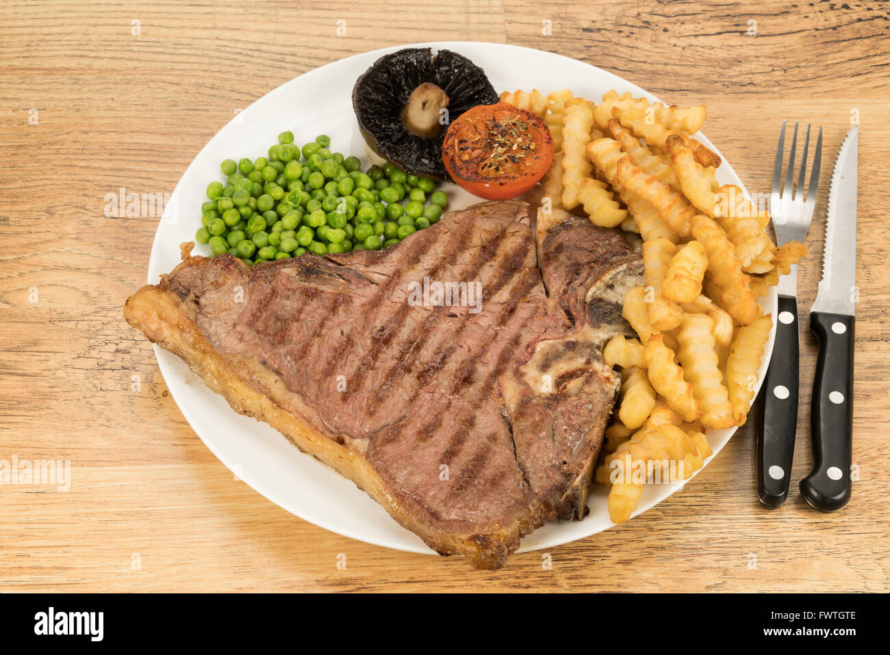 Un T-bone steak frites et le dîner avec des petits pois, champignons et tomates Banque D'Images