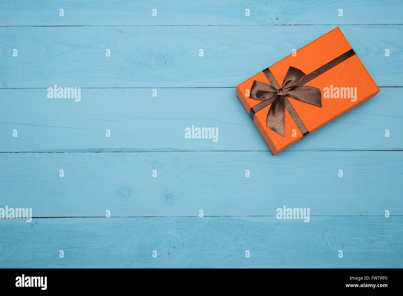 Boîte cadeau orange avec brown bow on a blue background Banque D'Images