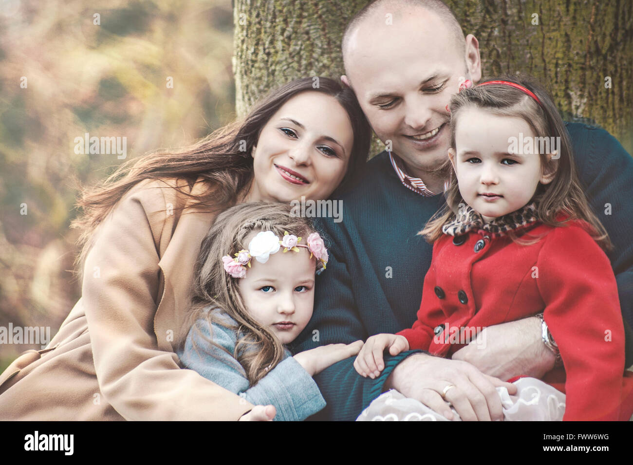 Les parents avec leurs deux petites filles se détendre sous tree in park Banque D'Images