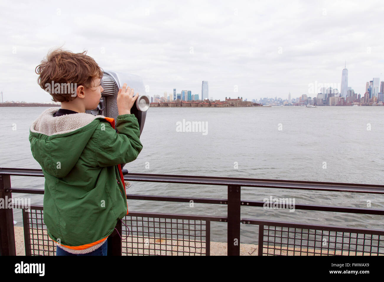 Un garçon de six ans à l'aide d'une paire de jumelles à monnayeur à Liberty Island, New York, États-Unis d'Amérique. Banque D'Images