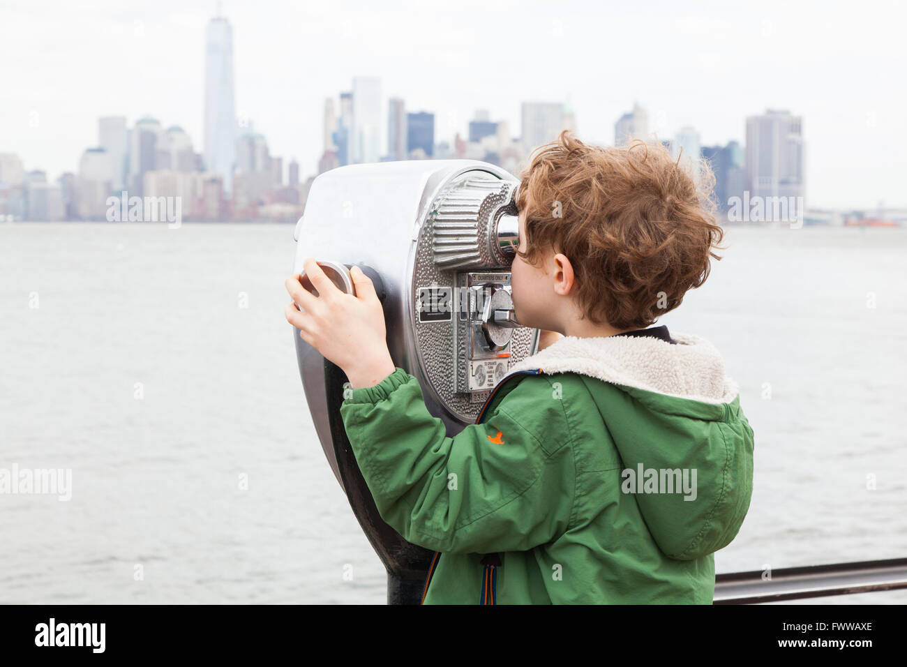 Un garçon de six ans à l'aide d'une paire de jumelles à monnayeur à Liberty Island, New York, États-Unis d'Amérique. Banque D'Images