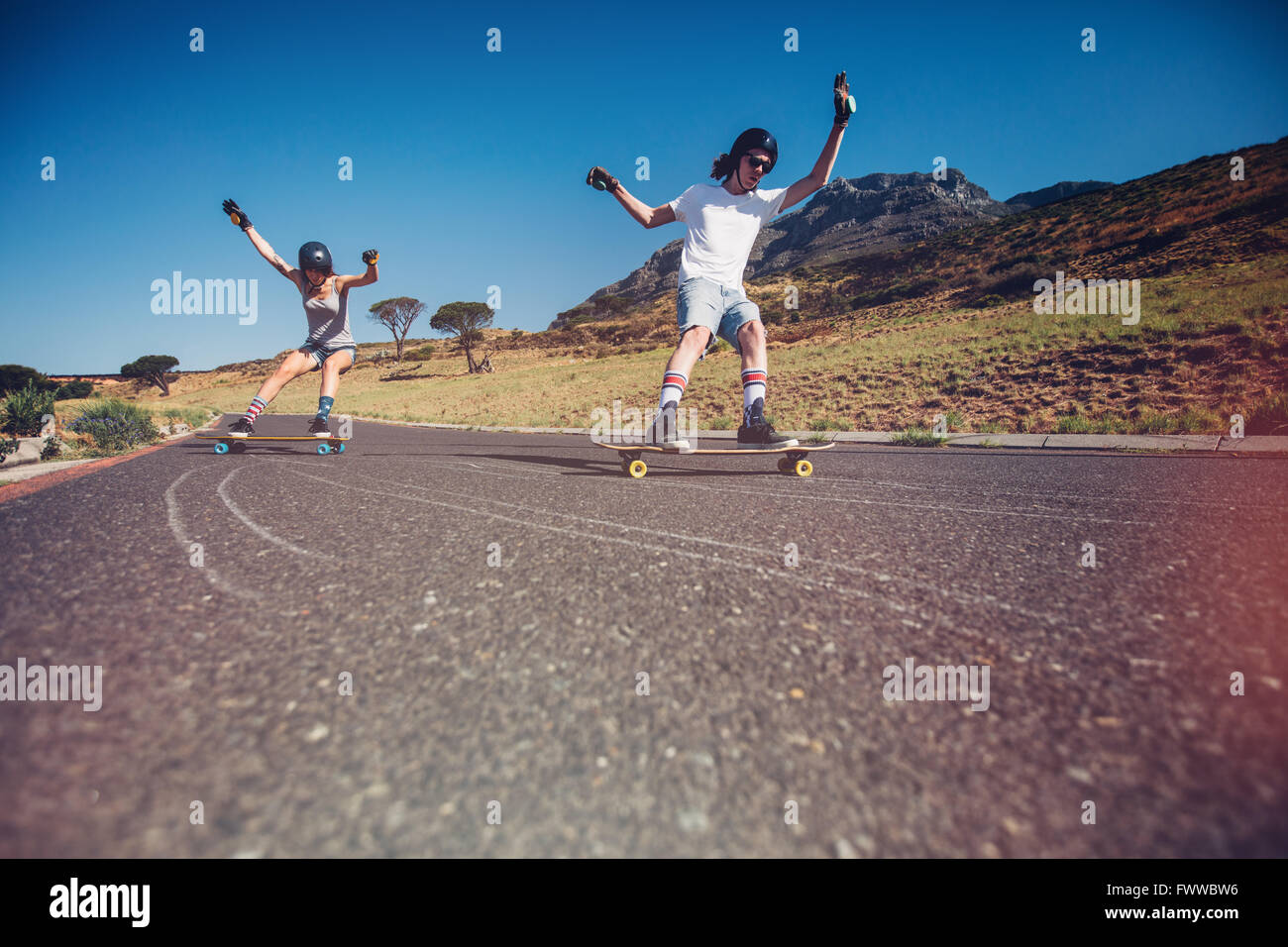 Jeune homme et femme de la planche à roulettes sur la route. Jeune couple practicing patiner sur une route ouverte. Banque D'Images