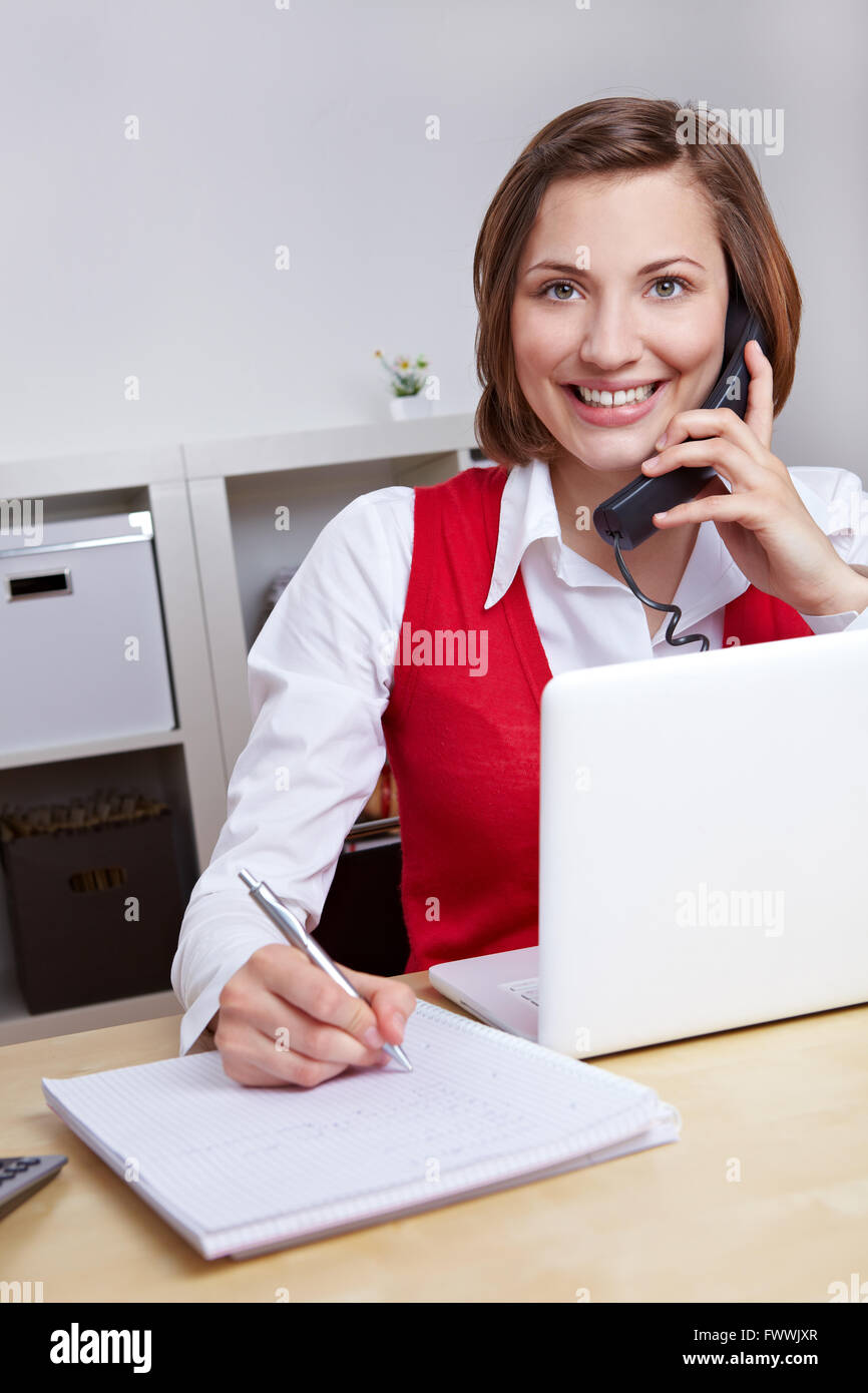 Heureux femme travaillant pour le centre d'appel hotline des notes lors d'un appel téléphonique Banque D'Images