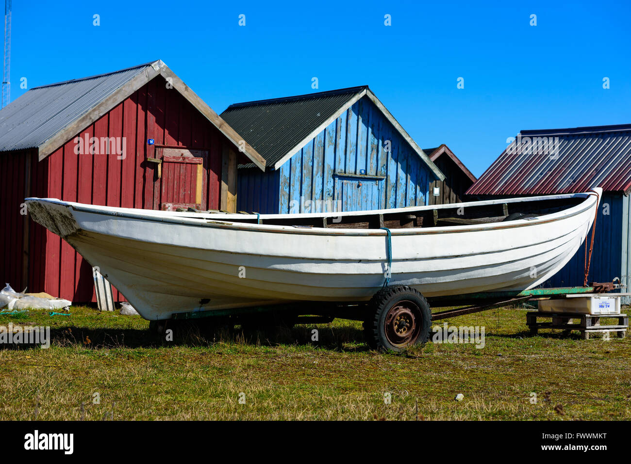 Simrishamn, Suède - 1 Avril 2016 : la chasse traditionnelle blanc canoë sur une remorque en face de cabines pêche rouge et bleu. Banque D'Images