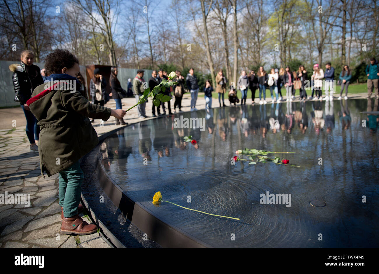 Berlin, Allemagne. Le 08 Avr, 2016. Un garçon jette une rose dans l'eau à la mémoire des Sinti et Roms victimes du national-socialisme en Allemagne, Berlin, 08 avril 2016. Le monument est situé dans le Tiergarten juste à côté du Bundestag et conçu par l'artiste Dani Karavan. Dans le cadre de "la Journée des Roms, Sinti et Roms ' demandent pour la solidarité en Europe. Photo : KAY NIETFELD/dpa/Alamy Live News Banque D'Images