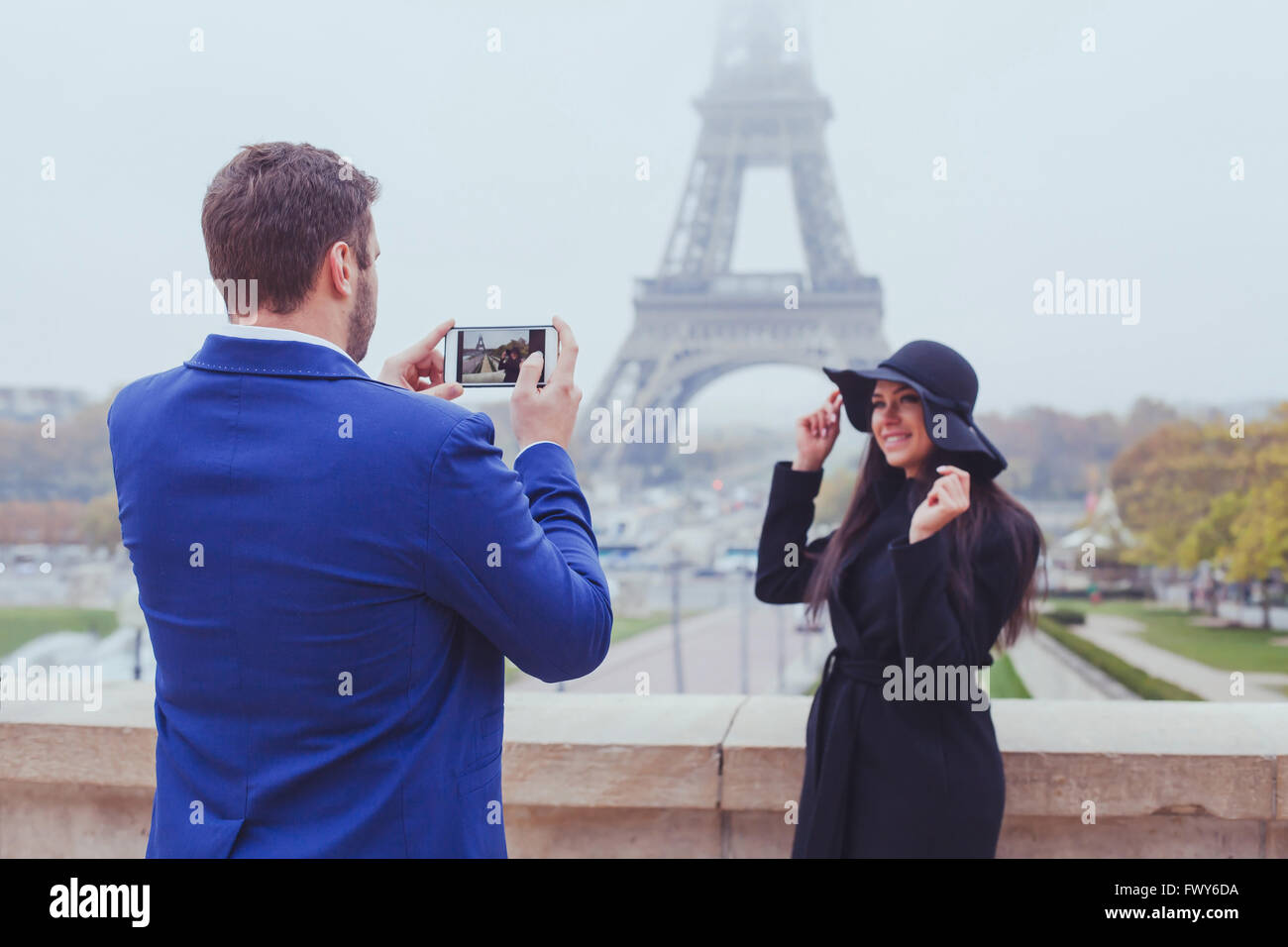 La photographie mobile, l'homme de prendre la photo d'une femme avec son téléphone, un couple de touristes près de la Tour Eiffel à Paris, France Banque D'Images