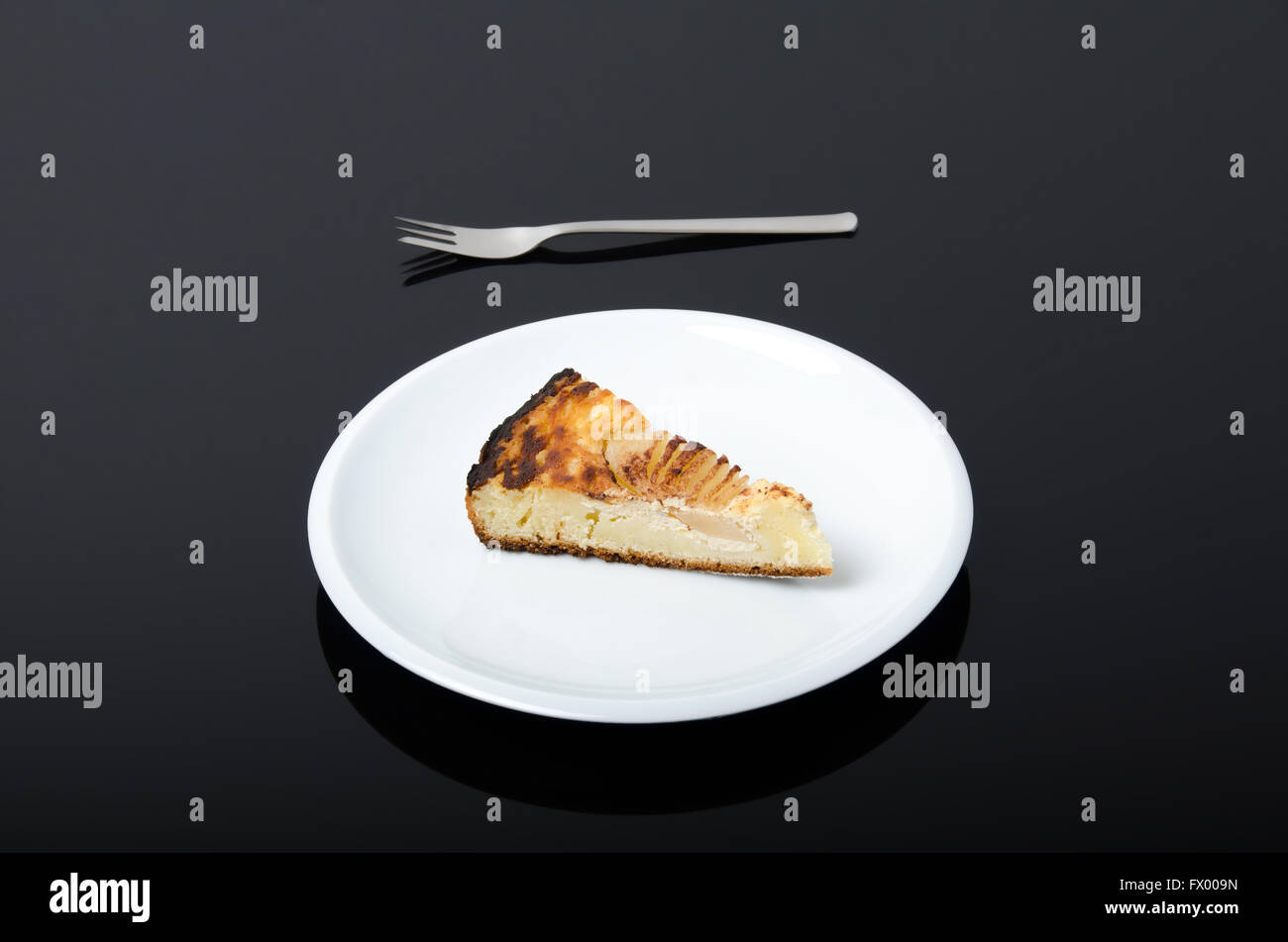 Plaque blanche avec morceau de tarte aux poires et à l'aide d'une fourchette à côté isolé sur fond sombre. Banque D'Images