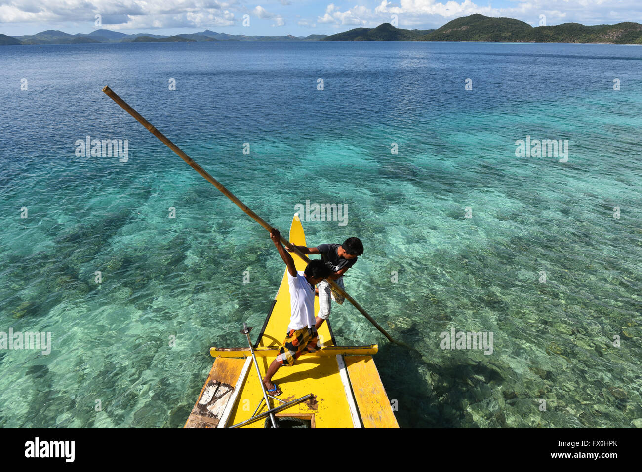 Les garçons d'El Nido, Palawan, Philippines poussant le bateau sur les récifs mis à explorer l'atmosphère reposante et crystal clear bay. Banque D'Images