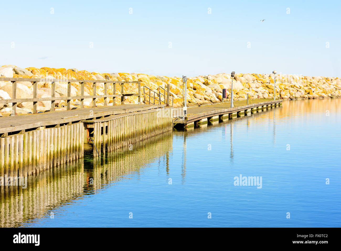 Jetée en bois juste à côté d'un grand quai de pierre. Le bois est un peu abîmé. L'eau est très calme sur cette journée de printemps sans vent dans le Banque D'Images