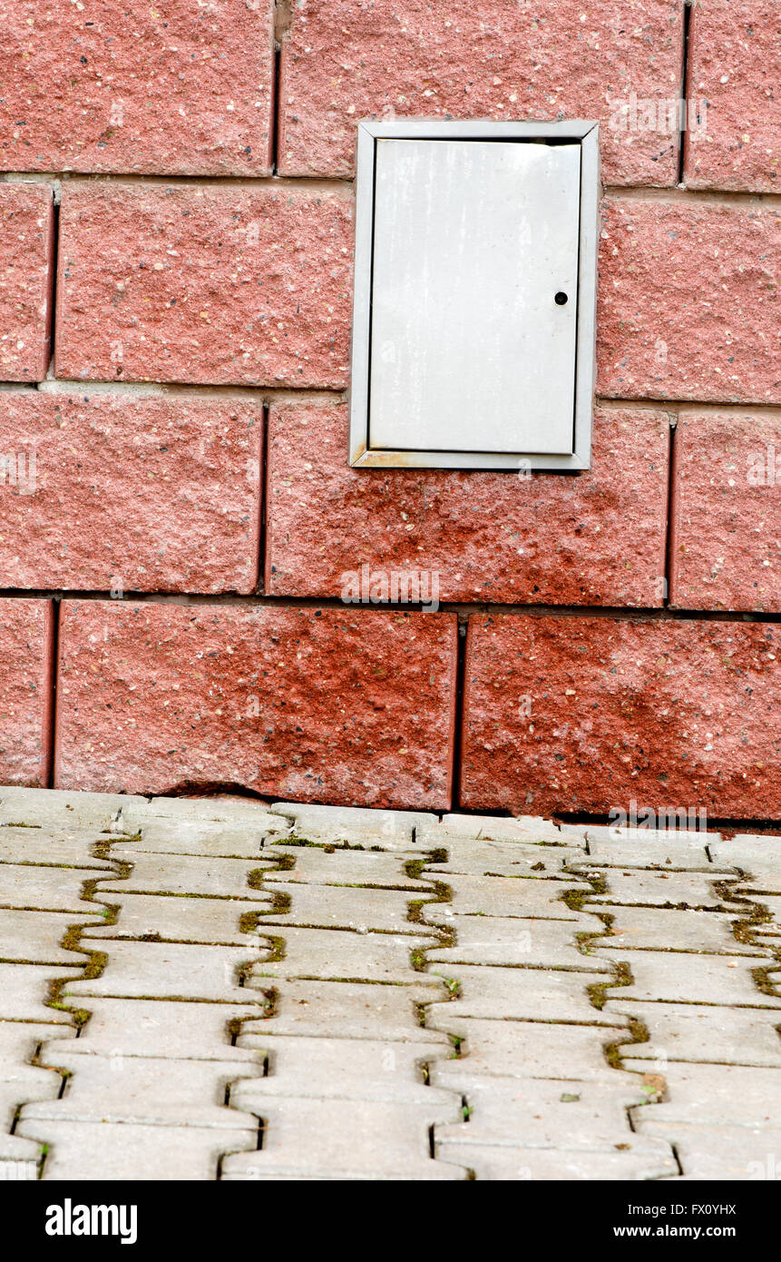 Le trottoir et le mur de blocs rouge humide avec standard téléphonique. Banque D'Images