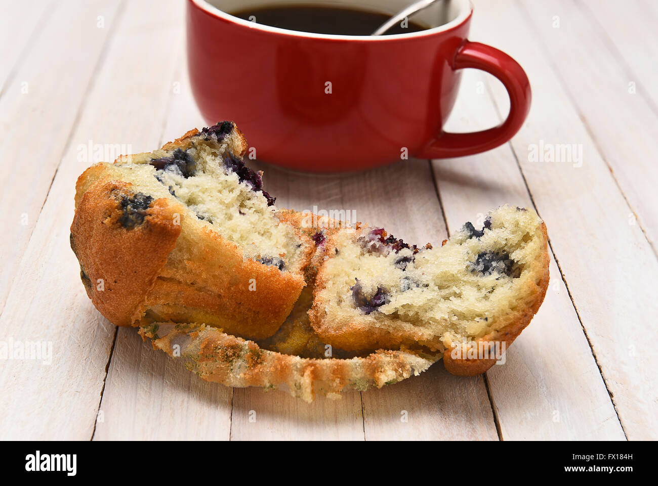 Libre d'un muffin aux bleuets avec une tasse de café dans l'arrière-plan. Le muffin est cassé en deux sur une table rustique en bois blanc. Banque D'Images