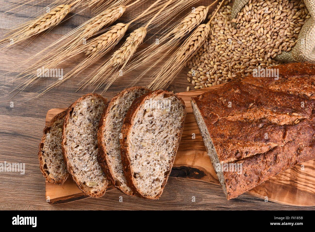 Vue de dessus d'une miche de pain multi céréales sur une planche à découper, un sac de jute de grain de blé et les tiges. Banque D'Images