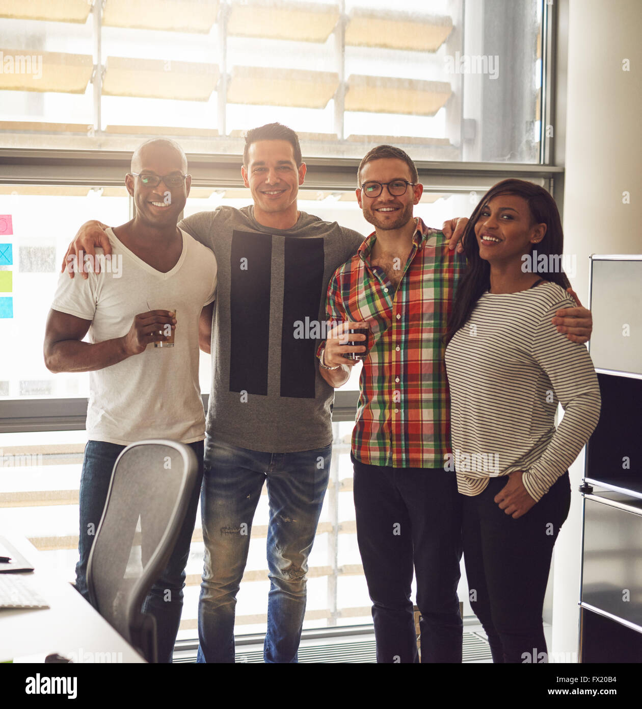 Groupe de quatre amis divers habillé dans des vêtements décontractés et des boissons tout en tenant debout près des autres, bureau avec la Banque D'Images