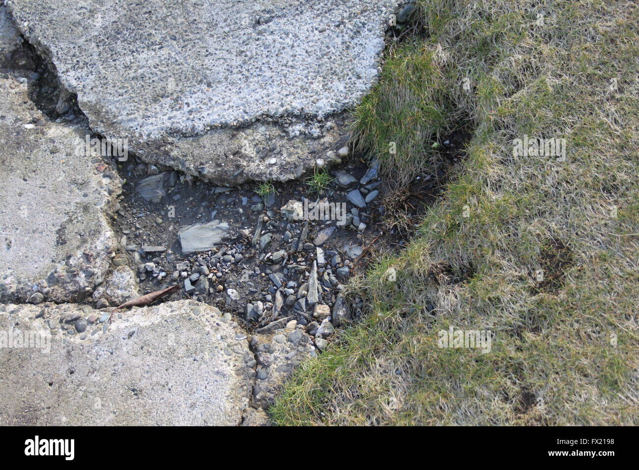 Close up d'un grand trou dans un revêtement en béton cassée à côté de Green grass court Banque D'Images