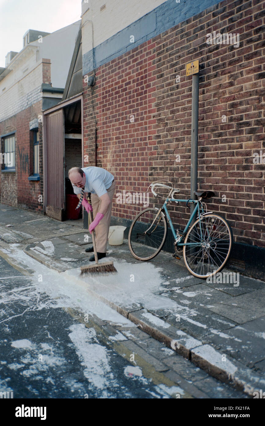 L'homme d'essayer de nettoyer la peinture de renversé en chemin england uk Banque D'Images