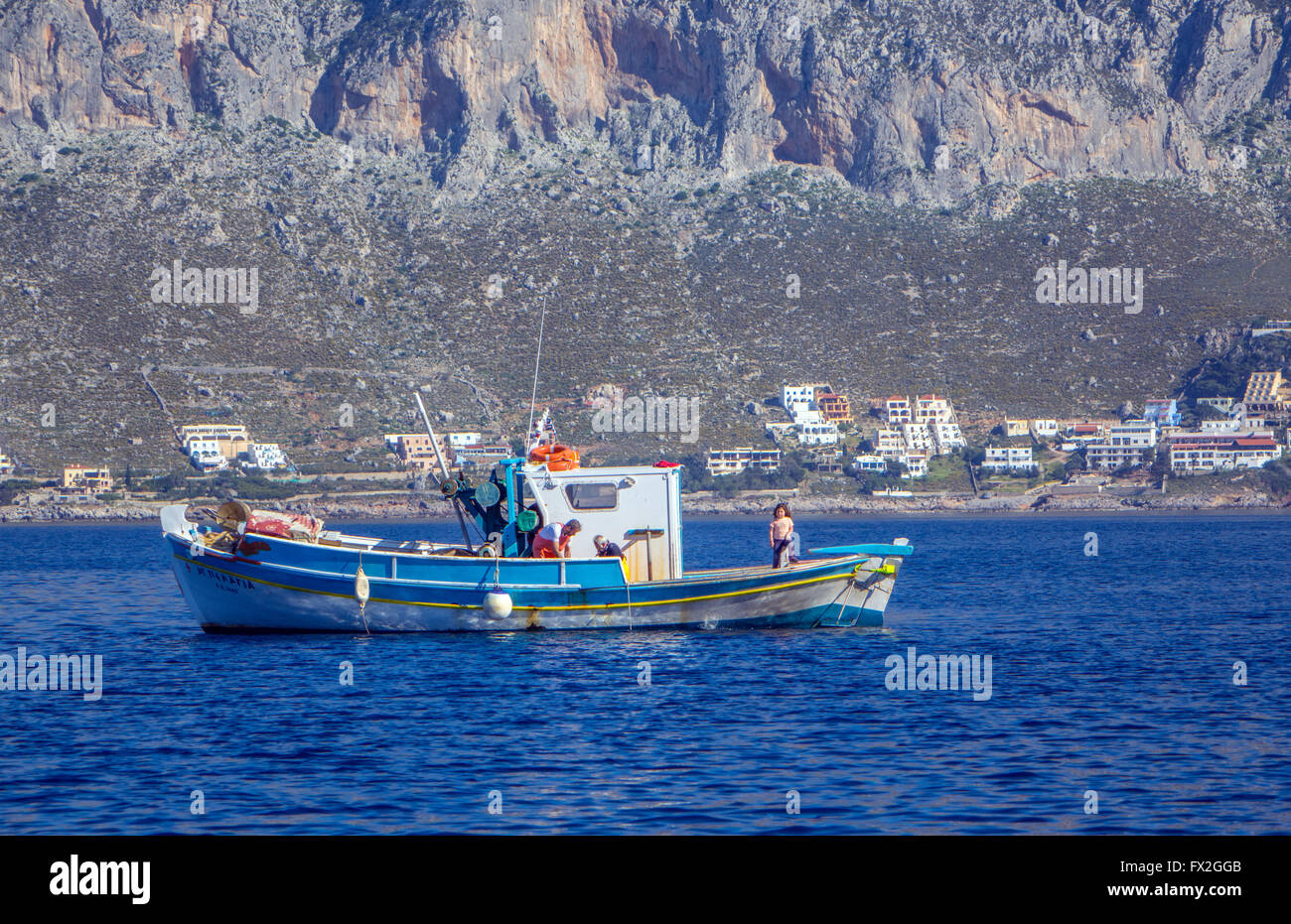 Bateau de pêche avec grecque bleue derrière rocky island Banque D'Images