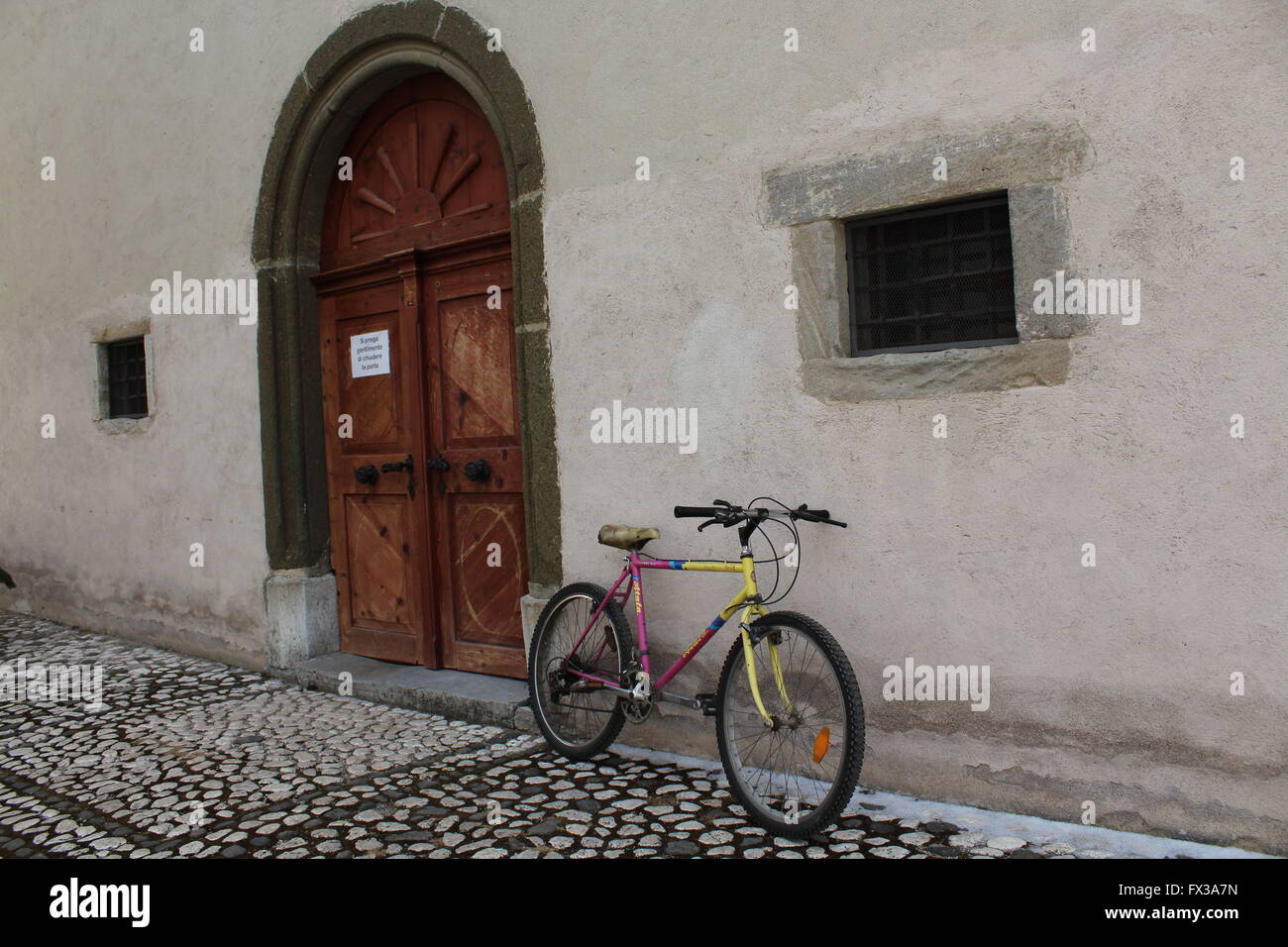Un vélo de montagne aux couleurs vives s'appuie contre un mur de l'église rustique dans la ville de Pozza di Fassa, Trentin, Italie Banque D'Images