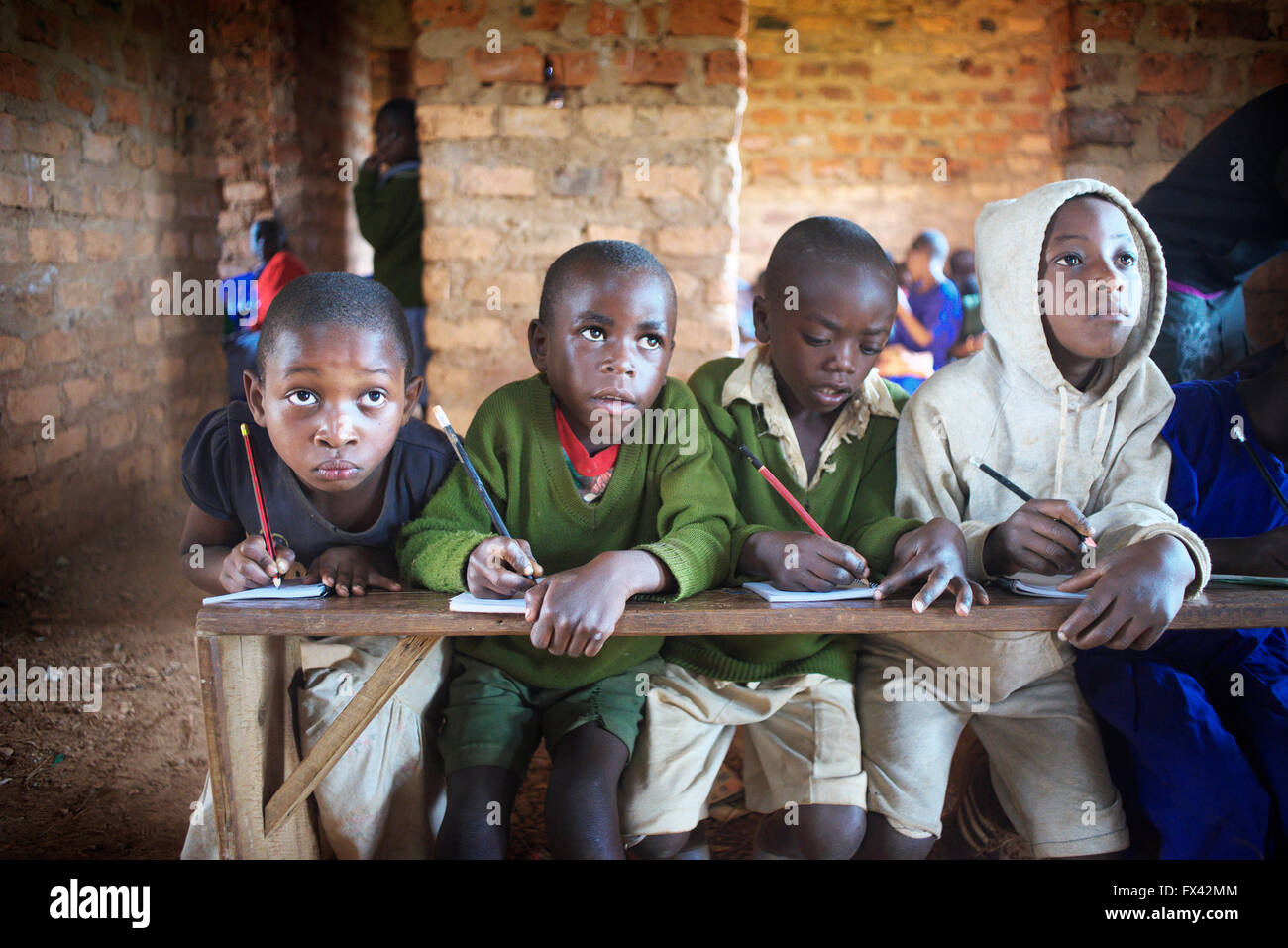 Groupe d'enfants dans les petites localités rurales école ougandaise s'asseoir sur un banc et l'étude en cours d'examens blackboard Banque D'Images