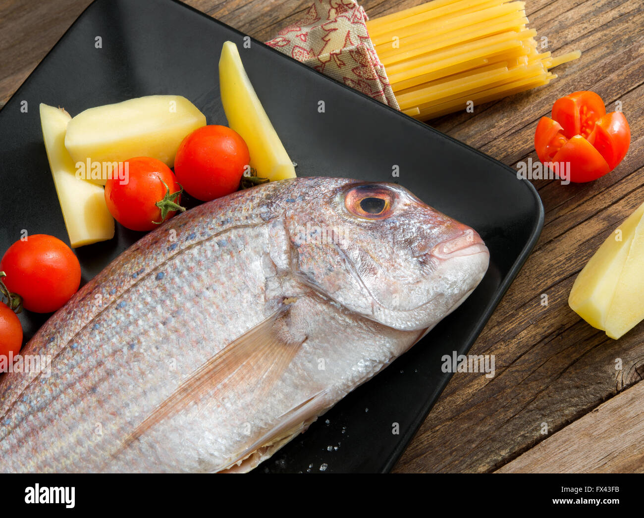 La brème de matières premières sur la plaque avec les pommes de terre, tomate et citron Banque D'Images