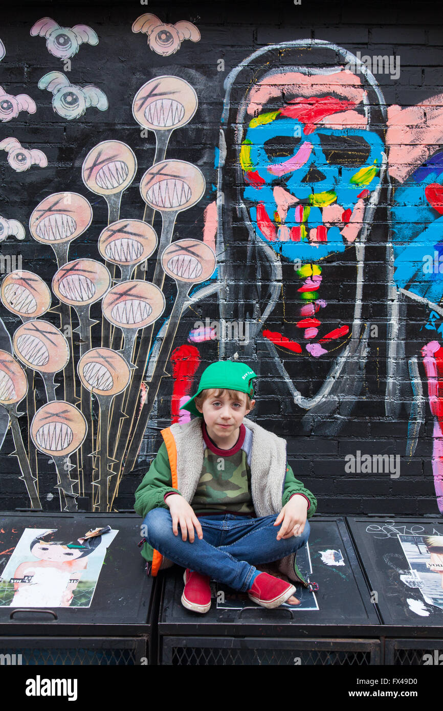 Six ans garçon assis à côté d'un mur de graffiti, Lower East Side, Manhattan, New York City, États-Unis d'Amérique. Banque D'Images
