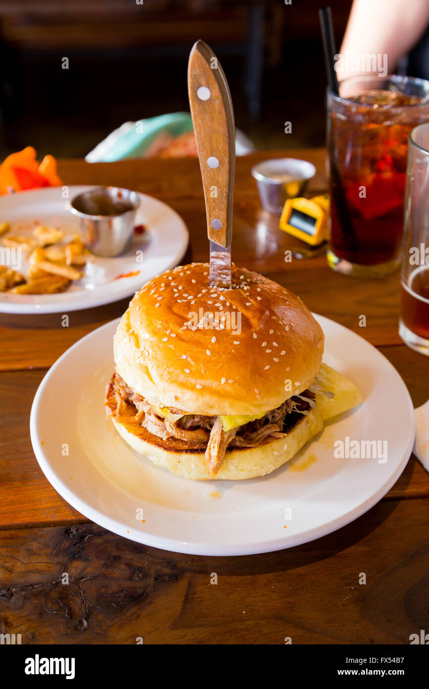 Ce sandwich ou un hamburger sur un petit pain sésame a un couteau dans le dessus de lui et a tiré le porc et les épices et la sauce cubaine sur elle. Banque D'Images