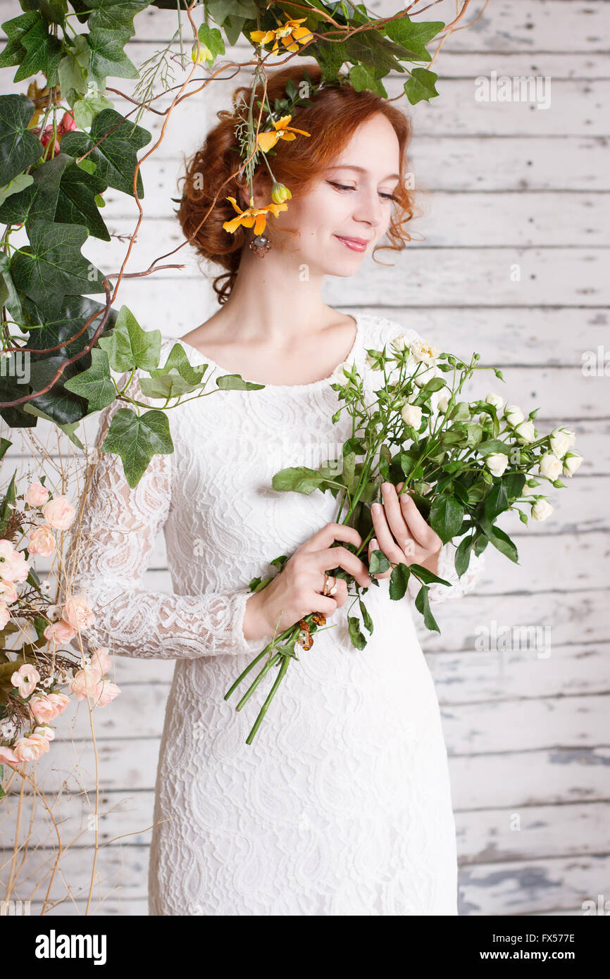 Les jeunes aux cheveux rouge mariée dans une robe en dentelle blanche et tient un bouquet de petites roses blanches. Banque D'Images