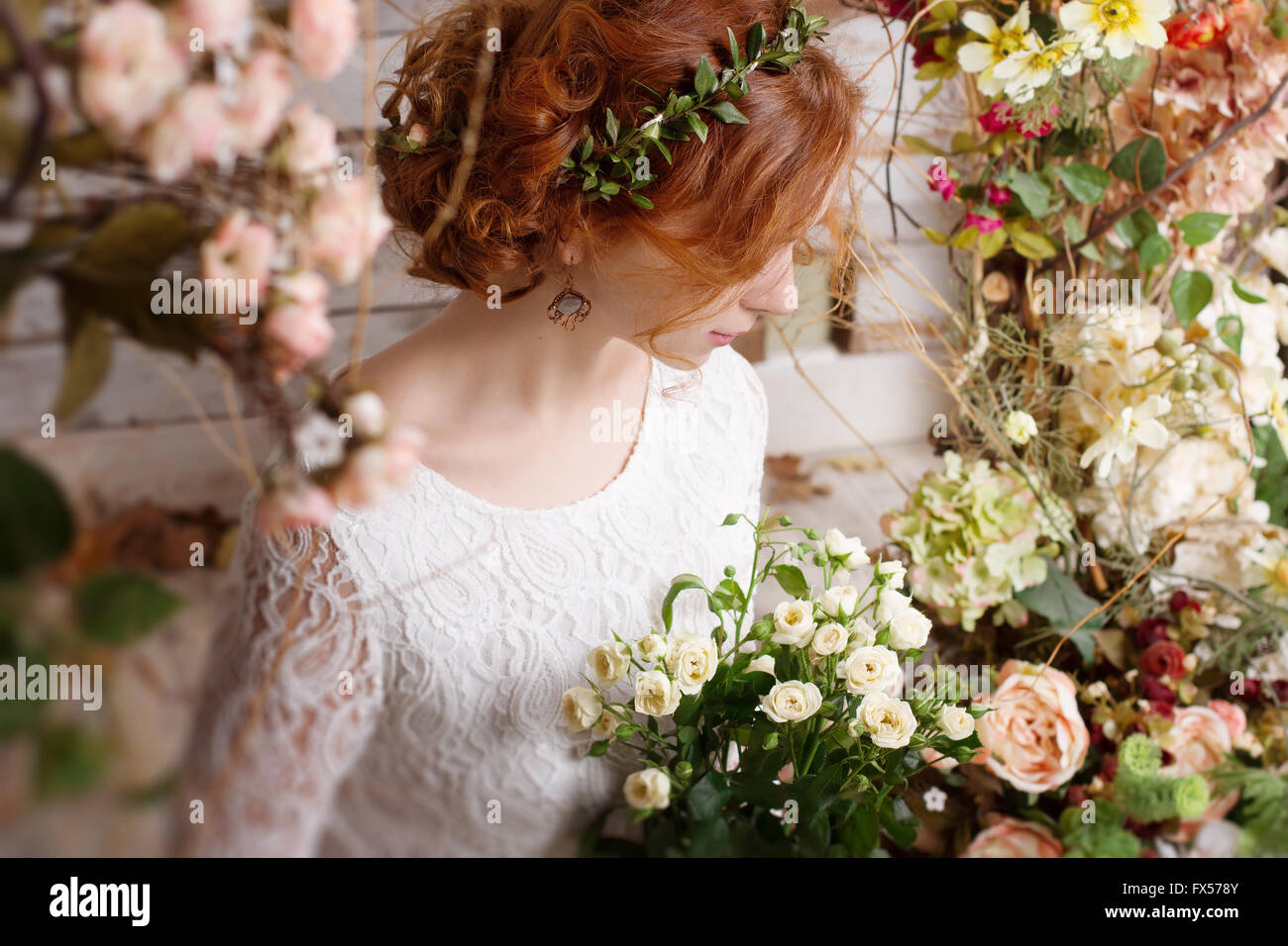 Portrait d'une jeune femme rousse dans une couronne verte, entourée de fleurs et plantes d'automne. Banque D'Images