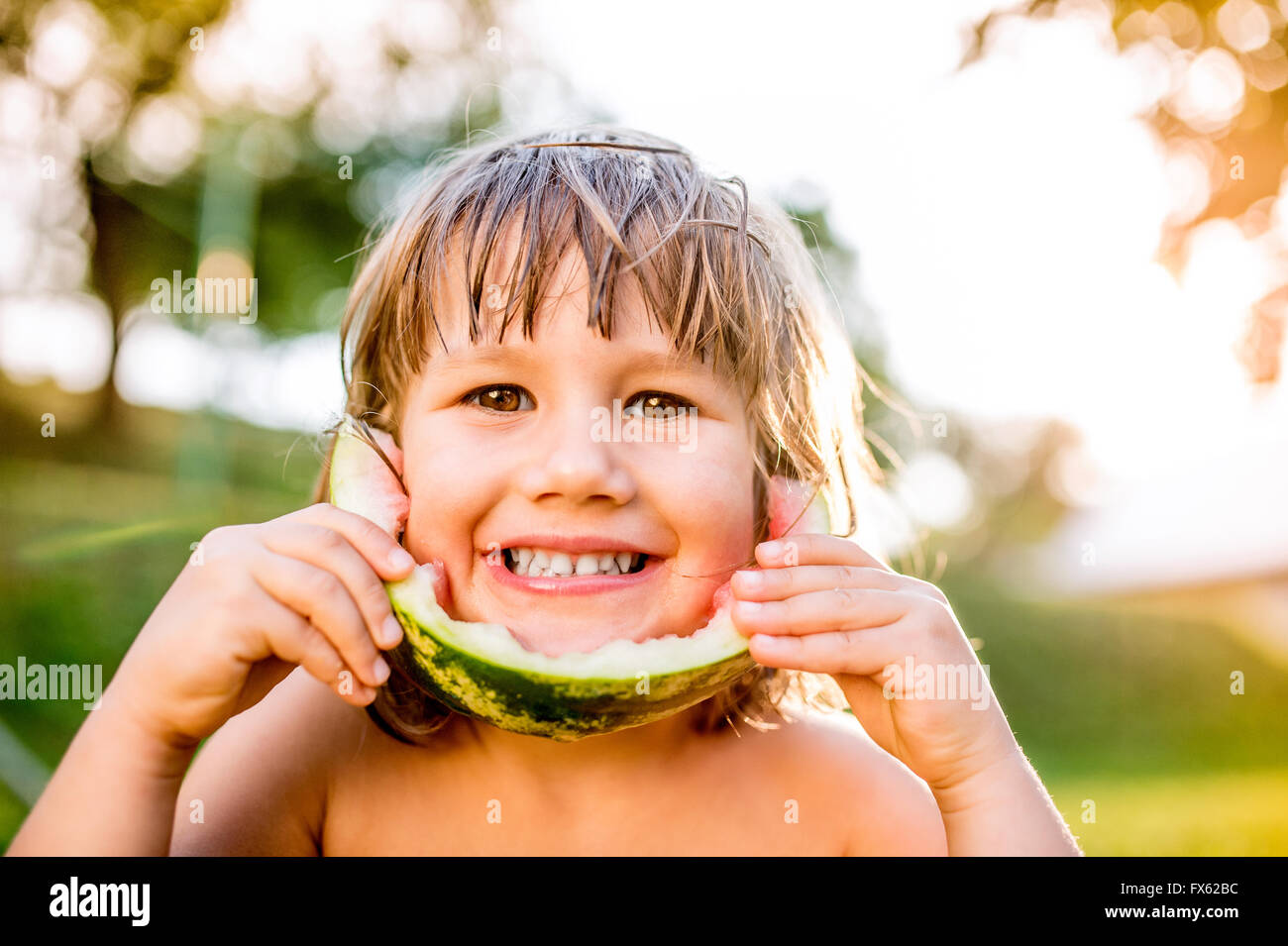 Cute little girl eating watermelon en jardin d'été ensoleillé Banque D'Images