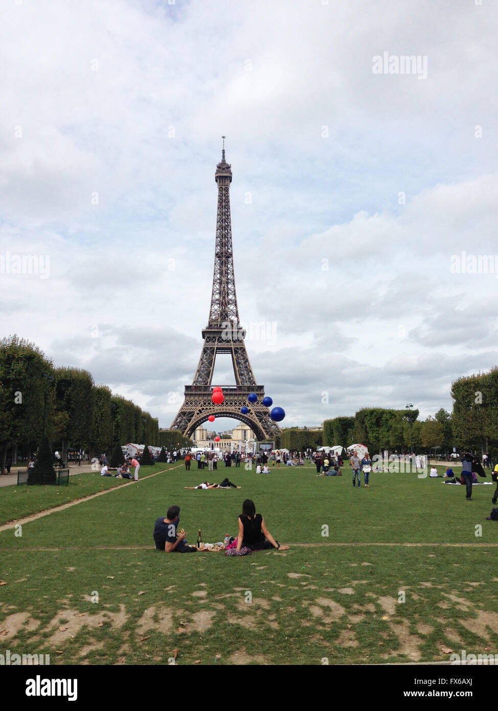 Les gens s'accrochent à l'avant de la tour Eiffel. Il y a des ballons bleus et rouges dans l'air. Un couple est un pique-nique. Banque D'Images