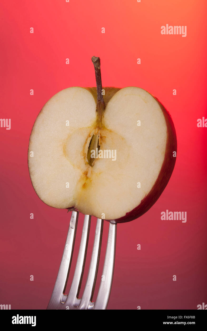 Red Apple réduit de moitié sur fourche avec fond couleur concept photo. Idéal pour une campagne ou d'adaptation de l'affiche. Banque D'Images