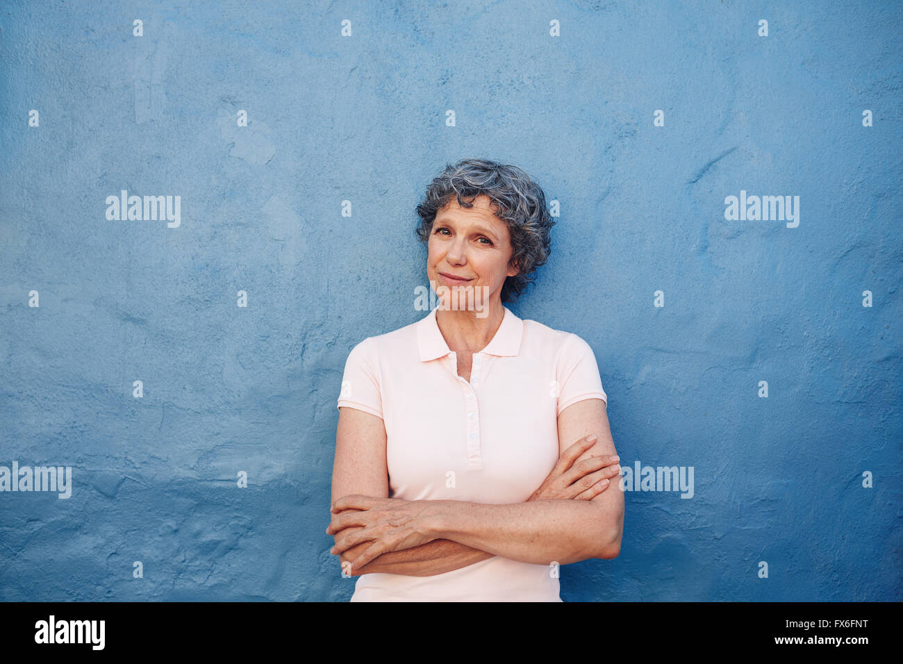 Portrait of senior woman standing magnifique avec ses bras croisés contre mur bleu. Mature female looking at camera. Banque D'Images
