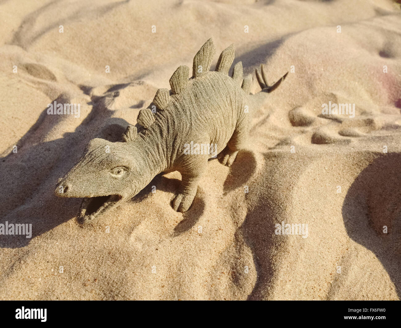 Jouet dans la forme d'un dinosaure debout sur le sable. Banque D'Images