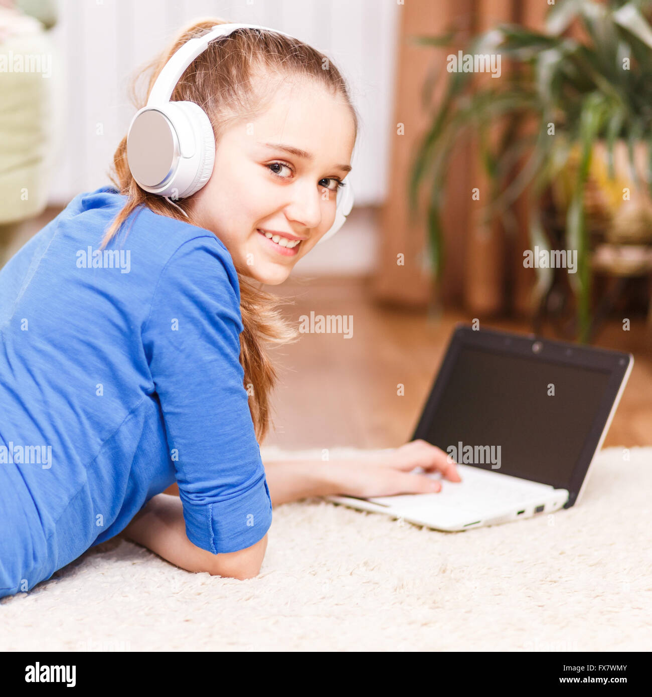 Teenage girl smiling avec casque blanc à l'aide de l'ordinateur portable sur le sol. Smiling adolescent avec ordinateur portable à la maison. L'éducation en ligne ba Banque D'Images